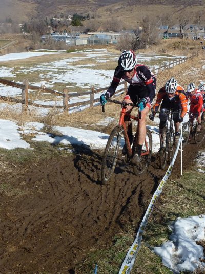 Group of cyclists on a cyclocross track riding their bikes up a hill with snow